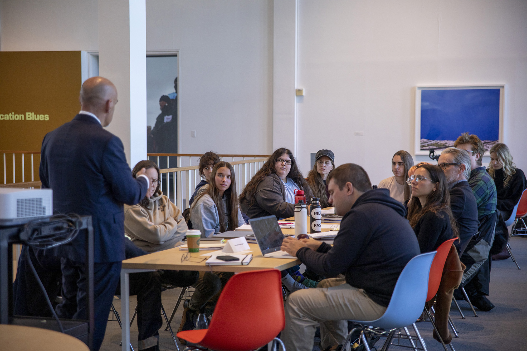 Man speaking to students seated at a table situated in the museum.